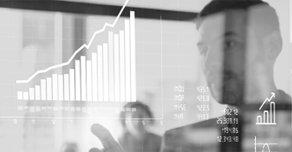 A person points at a transparent board displaying graphs and charts with increasing trends. Other people are visible in the background, suggesting a collaborative workspace.