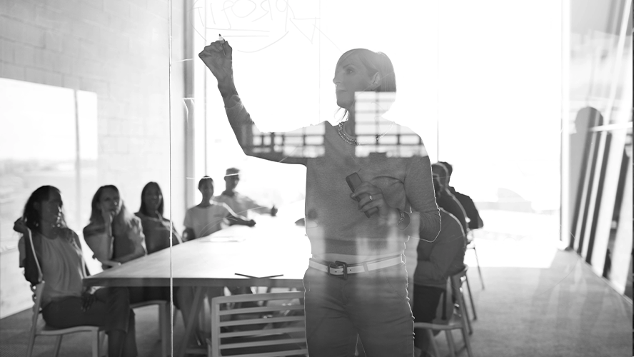 Woman presenting to a group in a boardroom with a glass wall.