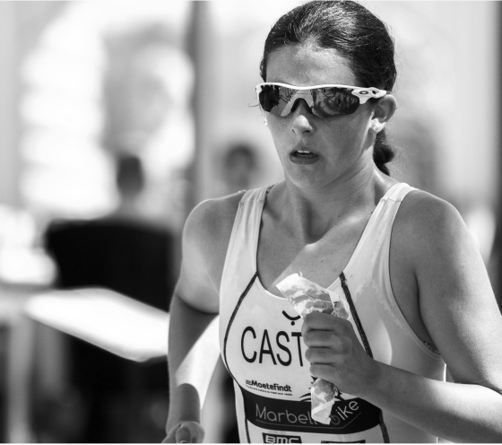 Woman in athletic gear and sunglasses running in a race, focused expression, black and white photo.