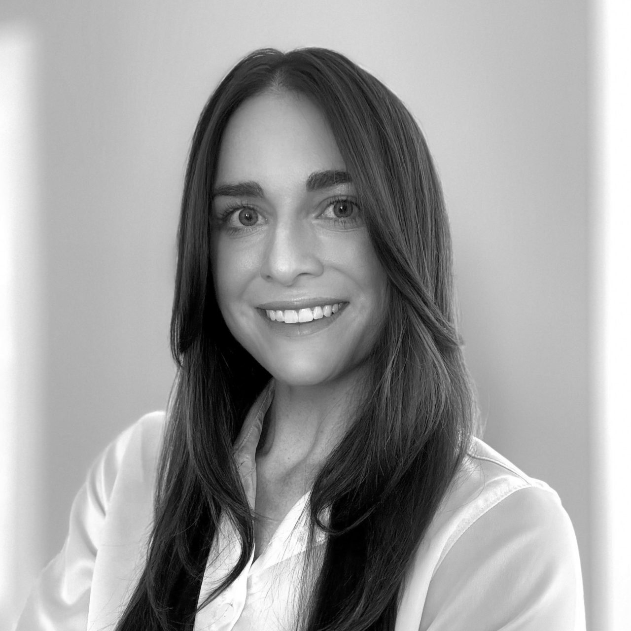 Black and white portrait of a smiling person with long, straight hair, wearing a light-colored blouse.