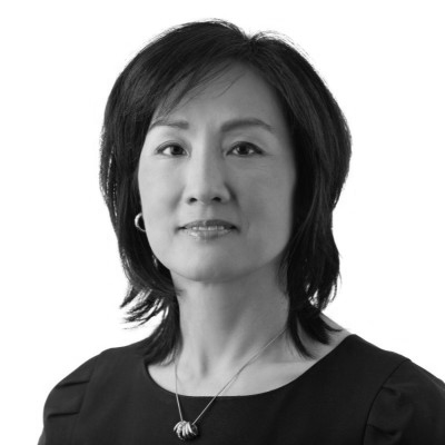 Professional portrait of an asian woman with short hair, wearing a black dress and a necklace, against a white background.