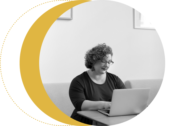 Person with curly hair sits at a table using a laptop, framed by a yellow crescent shape.