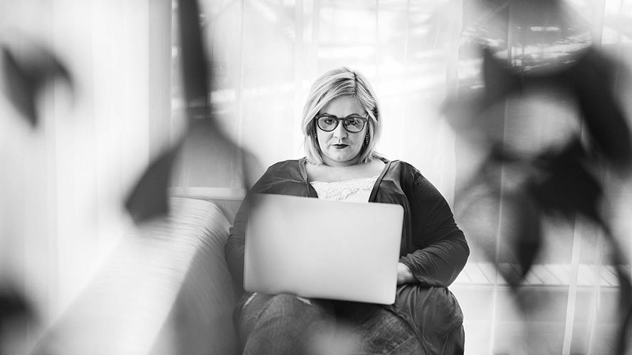 Woman with glasses sits using a laptop, in a blurred, backlit interior setting. black and white photo.