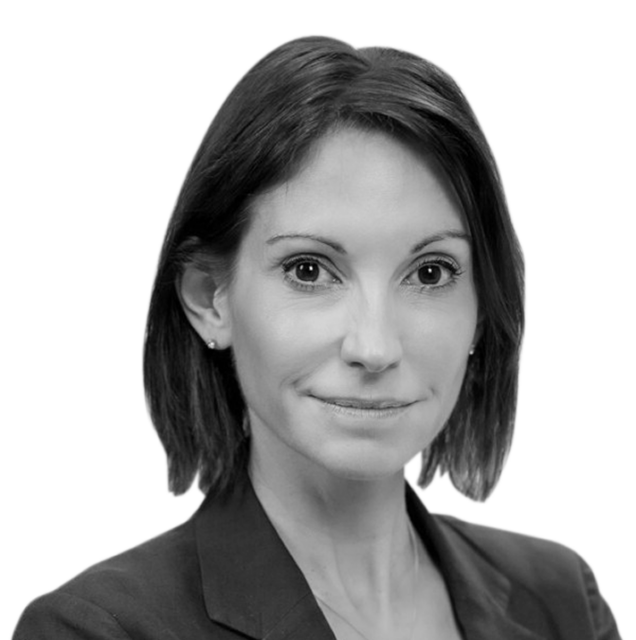 Black and white headshot of a woman with straight, shoulder-length hair, wearing a blazer. She is looking directly into the camera with a neutral expression.