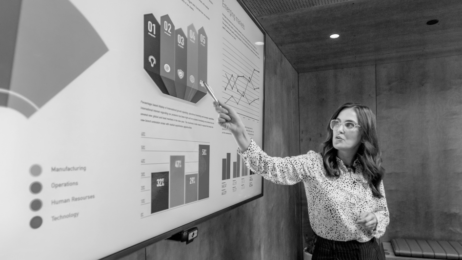 A person in glasses points to a presentation slide with various charts and graphs in an office setting.