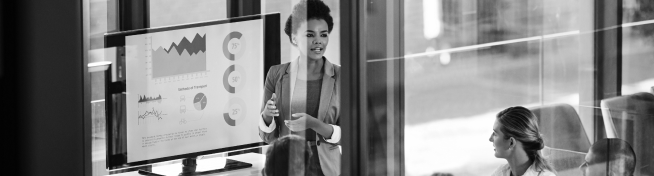 A woman presents data and graphs on a screen to three colleagues in a modern office.