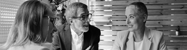 Three people in formal attire are engaged in a conversation around a table.