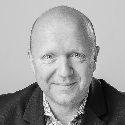 A bald man in a suit jacket and collared shirt smiles at the camera.