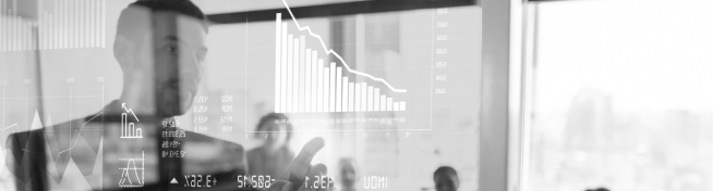 A person stands in front of a transparent screen displaying various graphs and charts during a presentation.