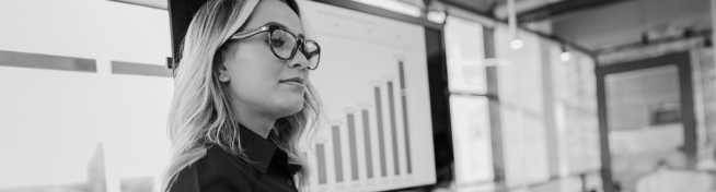 A person wearing glasses stands in front of a screen displaying a bar graph in an office setting.