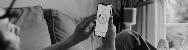 Person using a smartphone app to adjust the thermostat while sitting on a couch.