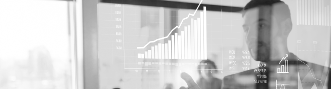 A person points at a transparent screen displaying bar graphs and line charts in an office setting.