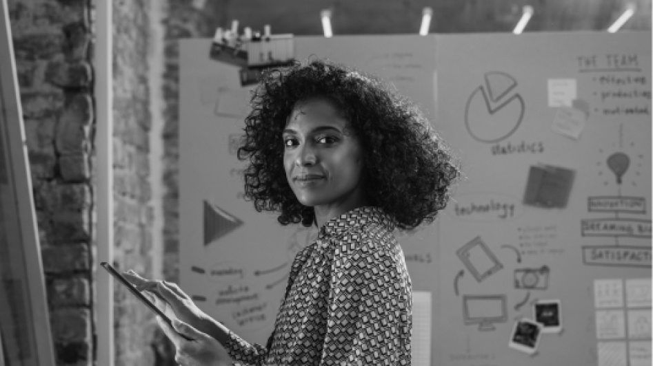 A person holding a tablet, standing in front of a whiteboard with charts and diagrams.