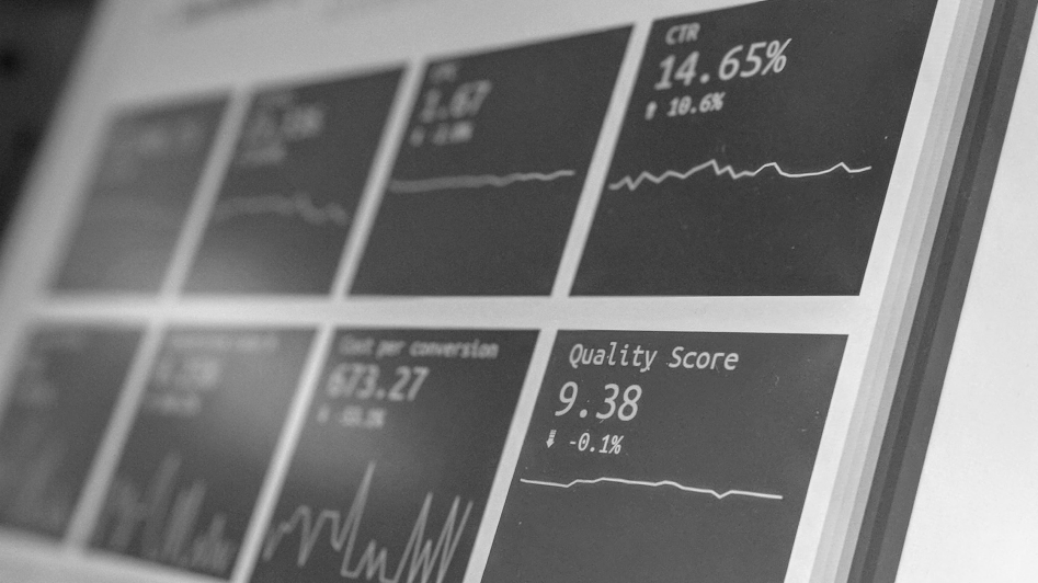 Monochrome close-up of a computer screen displaying various dashboard graphs and statistics, including CTR at 14.65% and Quality Score at 9.38.