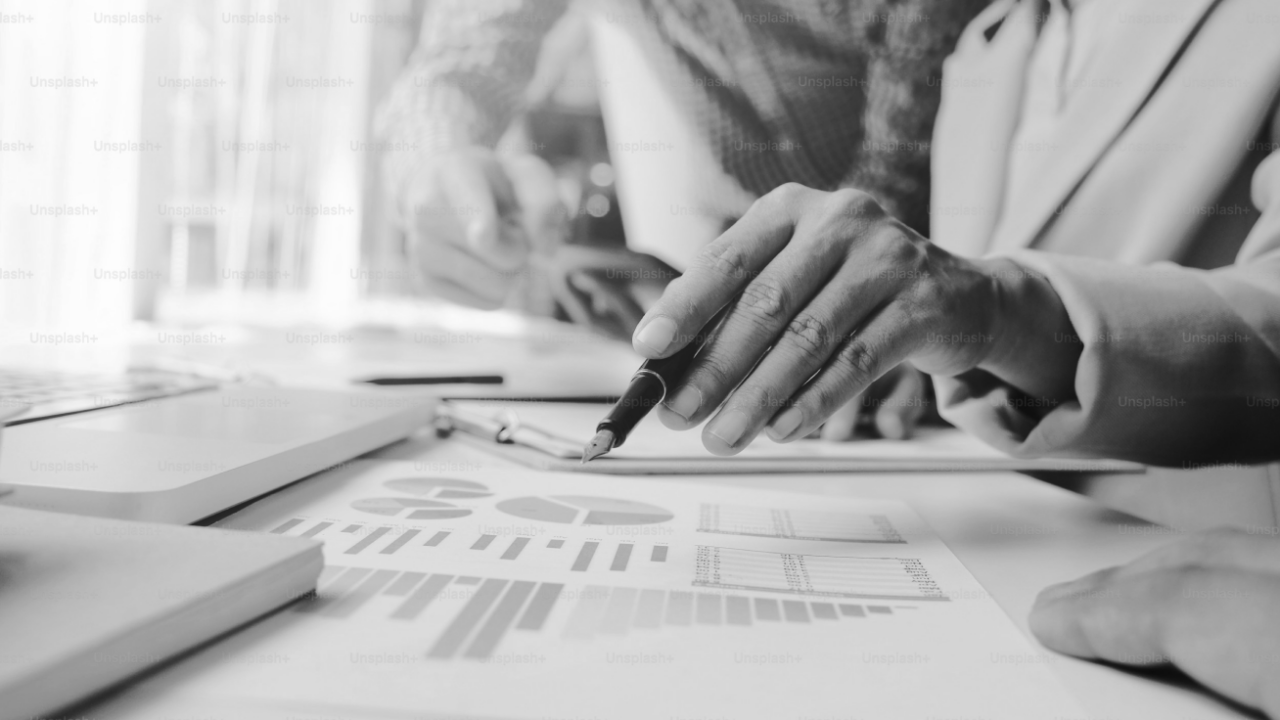 Two people reviewing charts and graphs on paper at a desk, one person pointing with a pen.