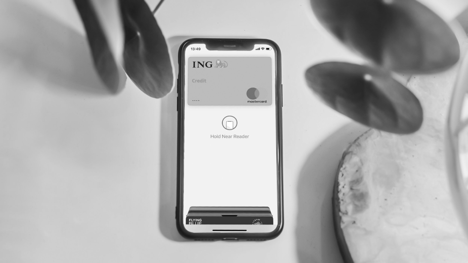 Smartphone displaying a digital credit card with NFC prompt on a white surface, surrounded by leaves.