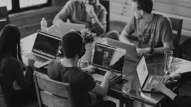 A group of people working on laptops around a table in a wooden room.