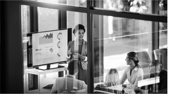 Person presenting data charts on a screen to colleagues in a modern office setting.