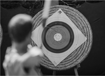 A person aims a bow at a target with multiple concentric circles.