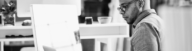 A person wearing glasses works intently at a computer in a modern office setting.