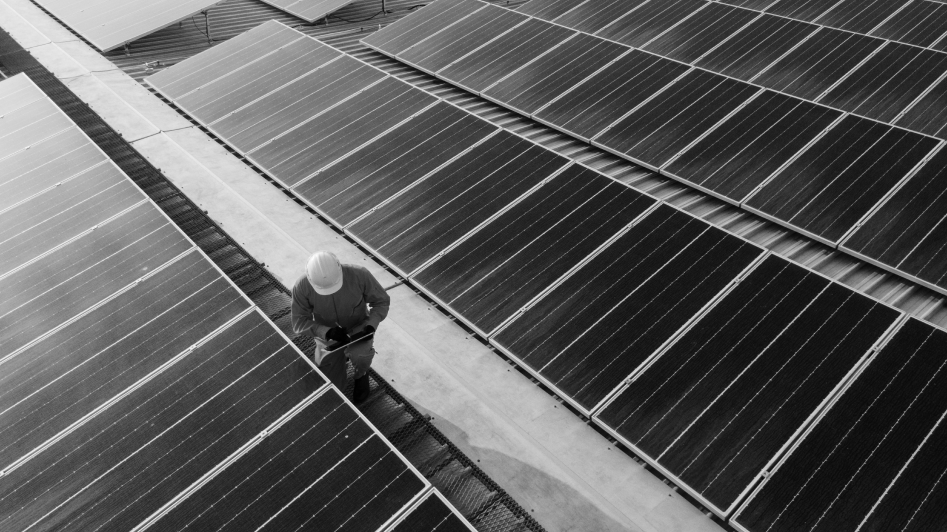 Person in a hard hat inspecting large solar panels on a rooftop.