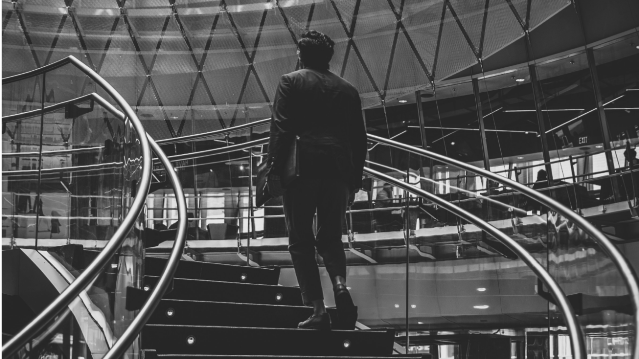 A person in a suit ascends a spiral staircase in a modern glass building.