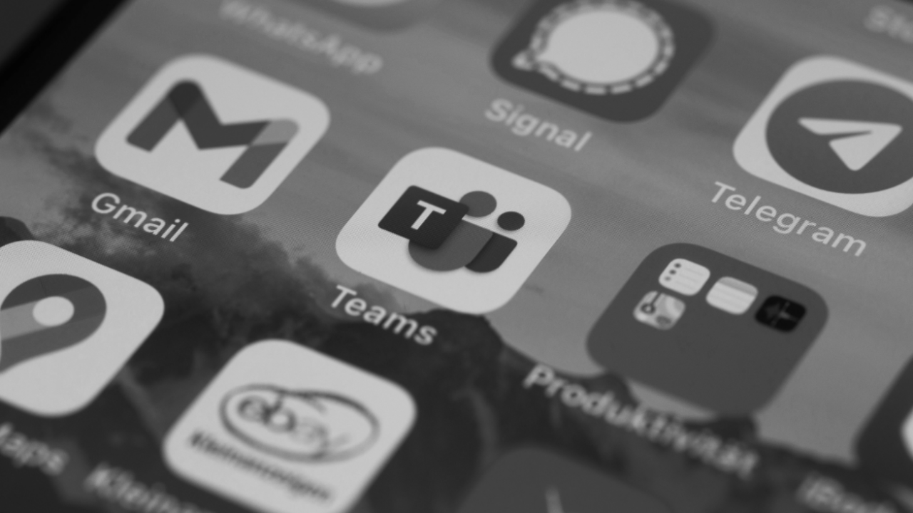 Close-up of a smartphone screen displaying icons for Gmail, Teams, Signal, Telegram, and other apps in grayscale.