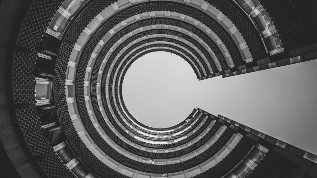 Black and white photo looking up at a circular building with concentric balconies and an open sky in the center.