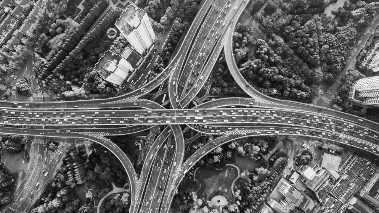 Aerial view of a large, complex highway interchange with multiple lanes and heavy traffic, surrounded by trees and buildings.