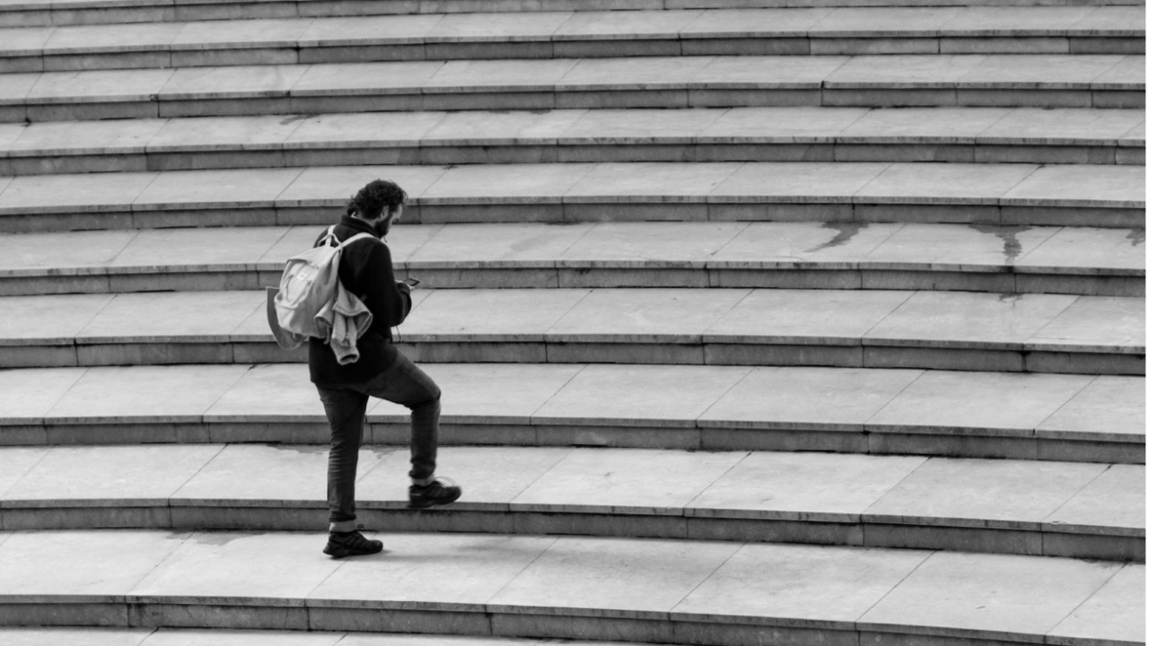 A person with a backpack walks up a set of wide, curved stone steps.