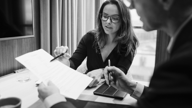 Two people in a meeting room reviewing a document, both holding pens.