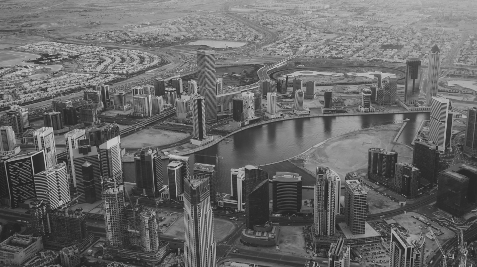 Aerial view of a city with tall buildings surrounding a winding river, featuring densely packed structures and roads in a desert landscape.