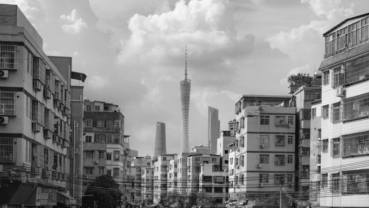 Black and white cityscape featuring a tall tower in the center, surrounded by various residential buildings under a cloudy sky.