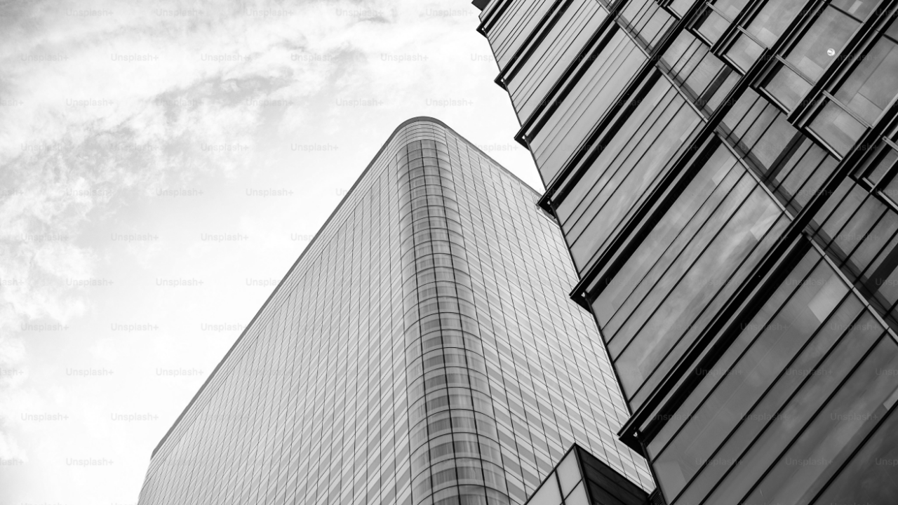 Black and white photo of modern glass skyscrapers from a low angle, highlighting sleek, curved architecture against a cloudy sky.