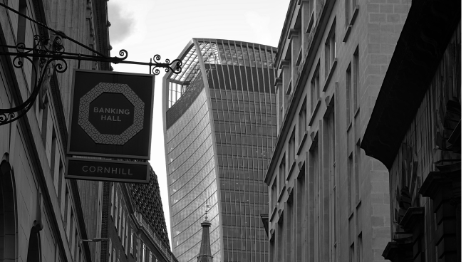 Black and white photo of a street view with tall buildings, featuring the modern curved architecture of the Walkie Talkie building in the background.